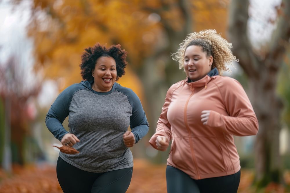Two happy chubby women jogging together in city park running adult determination.