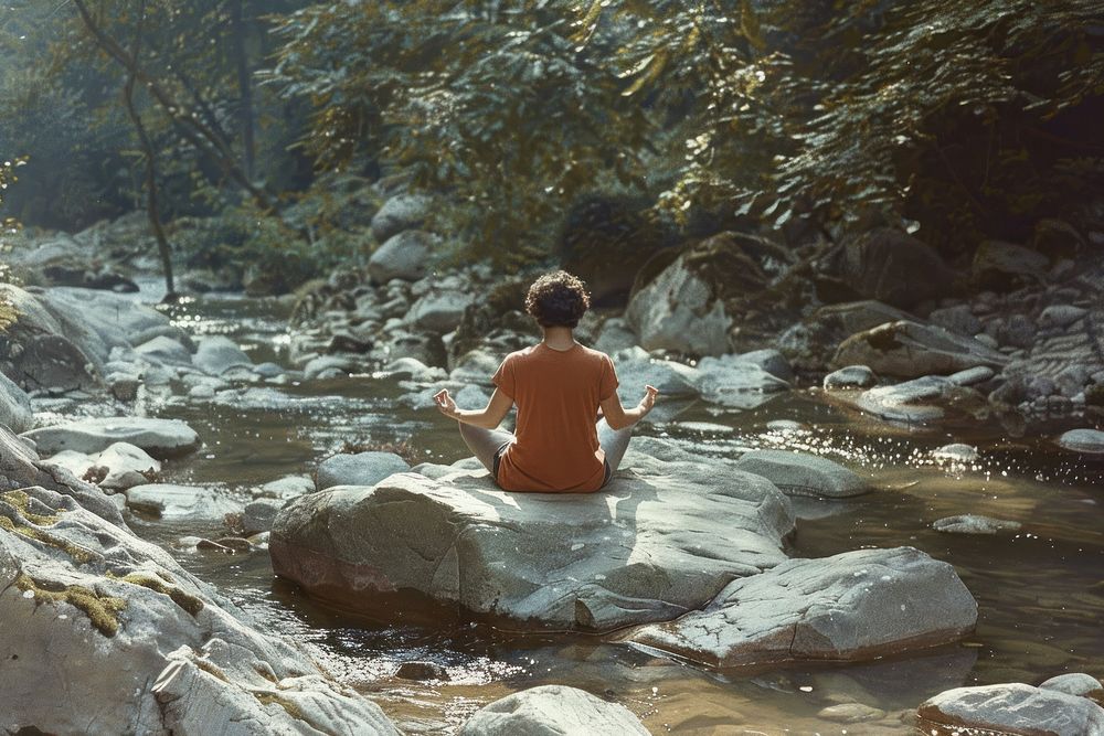 A person is meditating in the middle of nature rock vegetation outdoors.