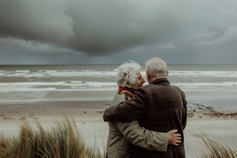 A photograph of an elderly couple standing on the beach sky photography shoreline.