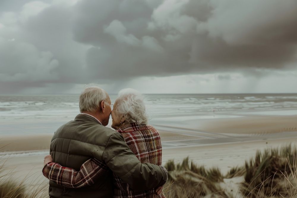 A photograph of an elderly couple standing on the beach cloud sky photography.