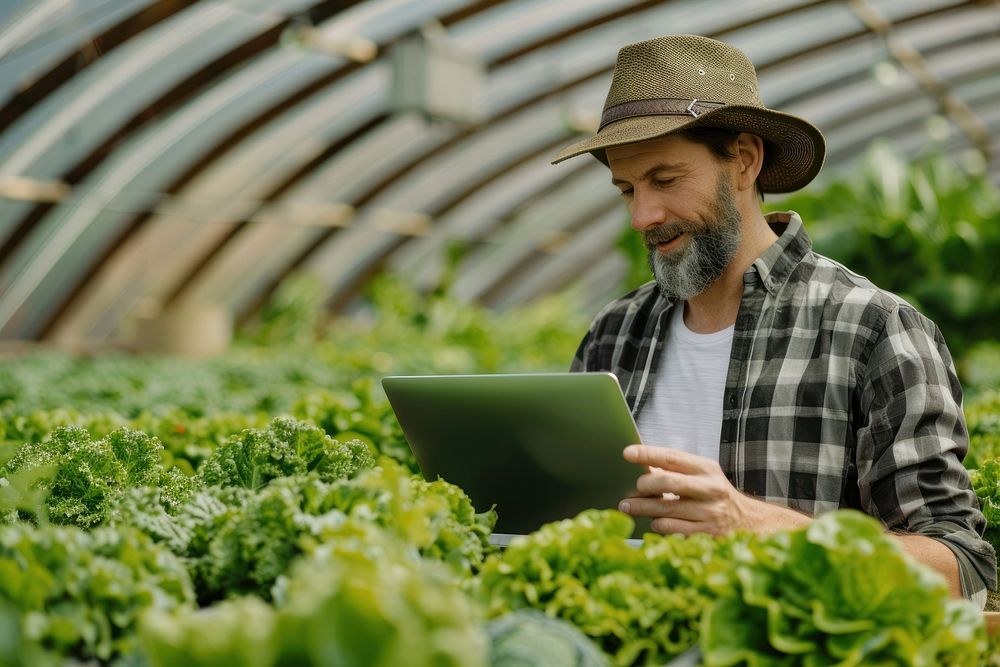 Male farmer using laptop male gardening outdoors.