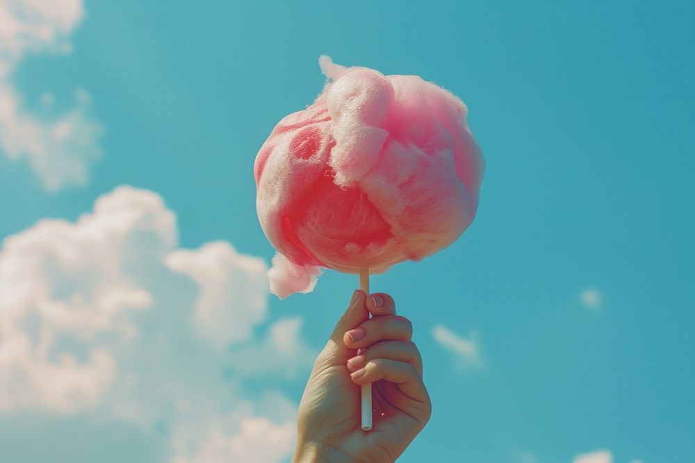 The hand of women holding pink cotton candy in the background of the blue sky confectionery sweets person.