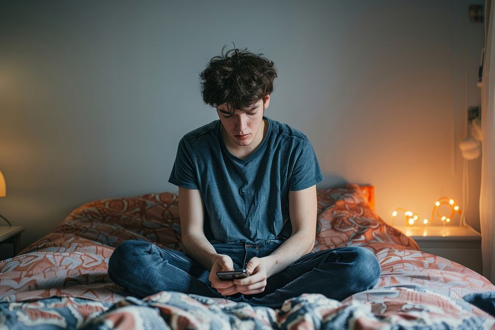 Sad thin man holding a mobile phone sitting bed electronics.