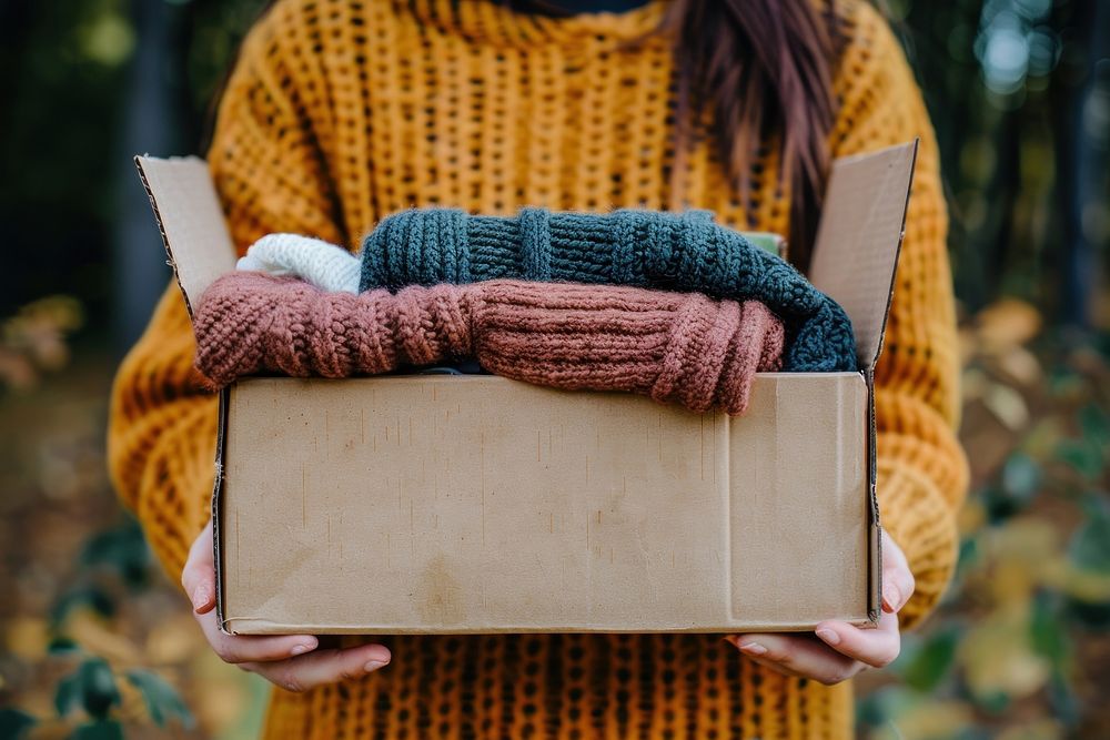 Hands holding carton box clothing knitwear apparel.