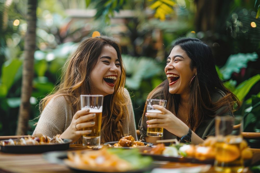 Two happy female having meal and beer and laughing drink party fun.