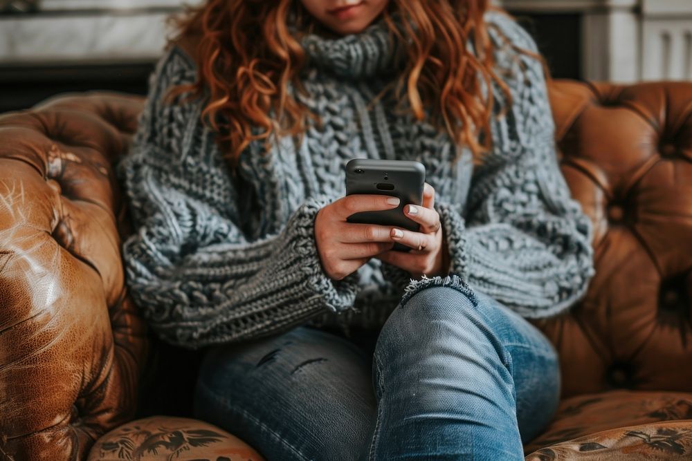 A woman sitting on sofa and playing smartphone in the living room electronics clothing knitwear.