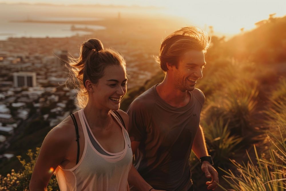 Fit young couple smiling while out for a run together on a scenic trail overlooking a city at sunset adult togetherness…