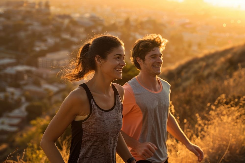 Fit young couple smiling while out for a run together on a scenic trail overlooking a city at sunset togetherness…