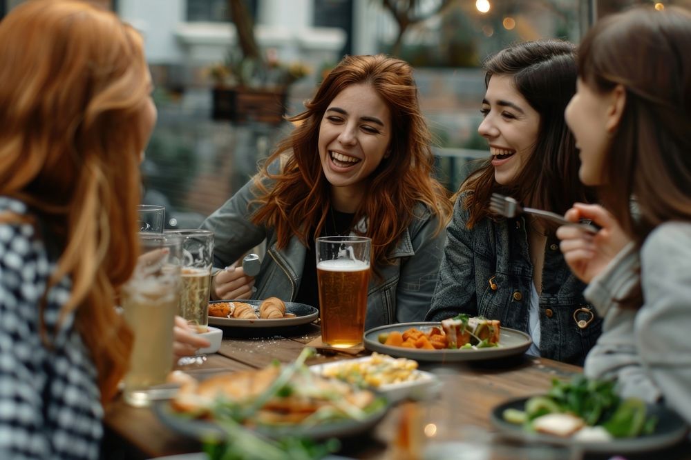 Happy female friends having meal and beer and laughing brunch drink party.