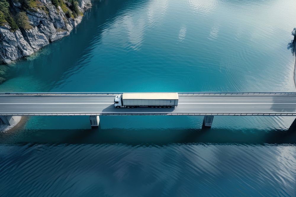 White semi truck driving on bridge crossing blue lake transportation outdoors vehicle.