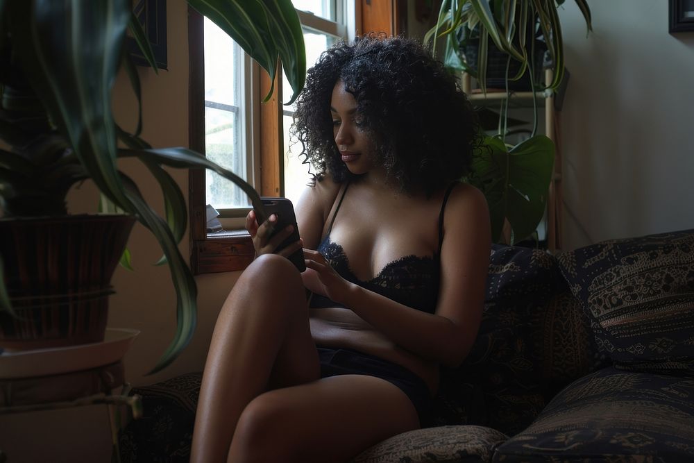 A black woman sitting on sofa and playing smartphone in the living room electronics furniture female.
