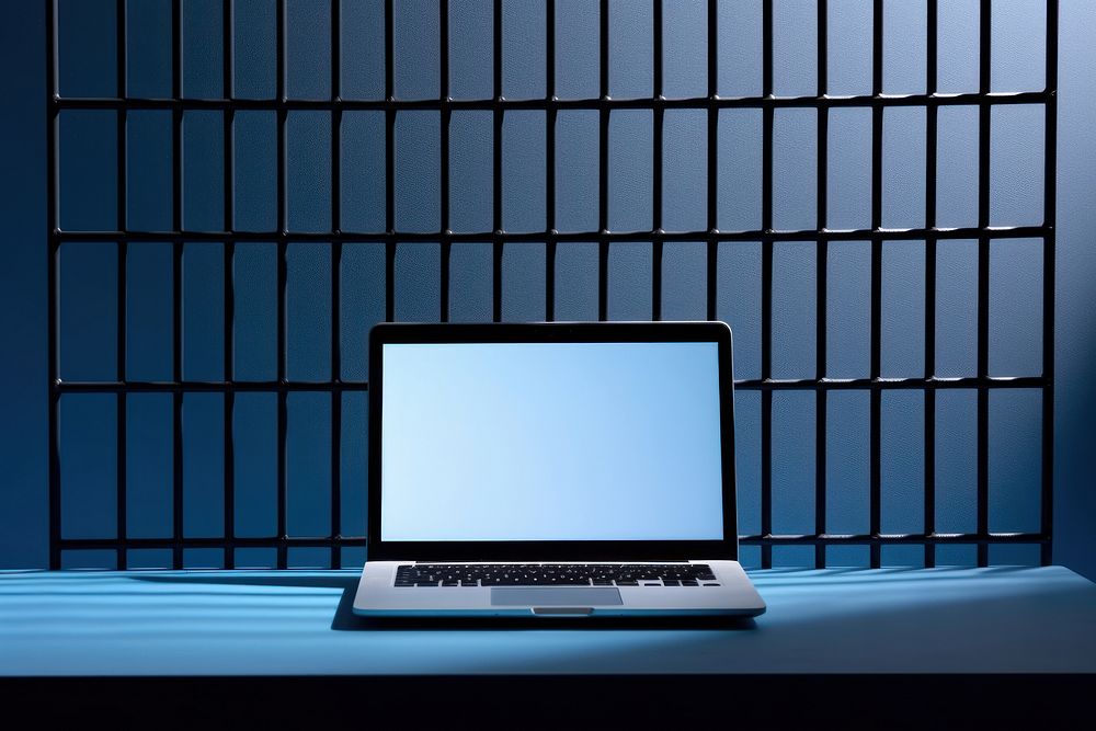 A laptop is on a black grid fence computer blue wall.