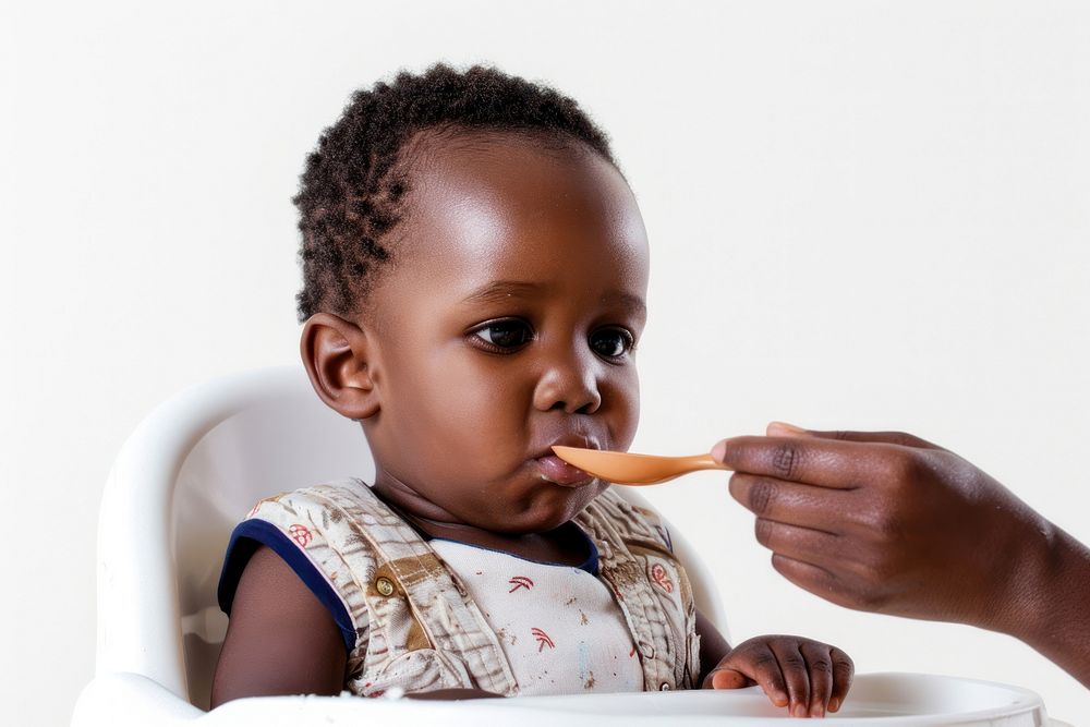 African American toddler sitting in a high chair food toothbrush biting.