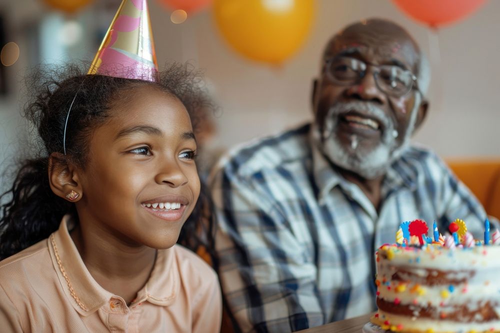 African Grandfather watching Hispanic girl eating birthday cake party hat accessories.
