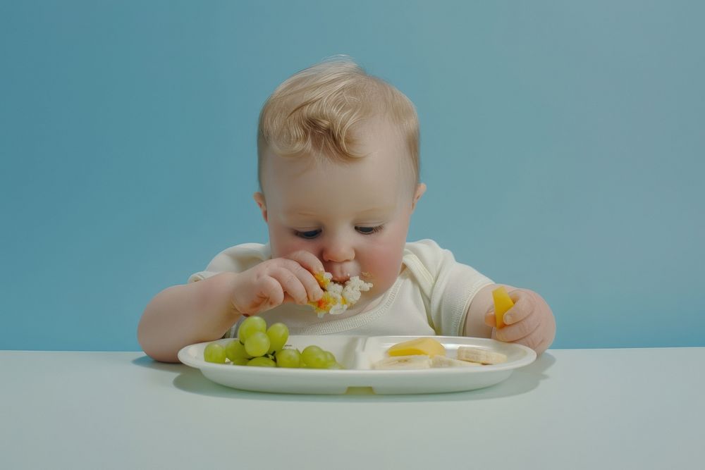 A baby is sitting at a table eating plate food.