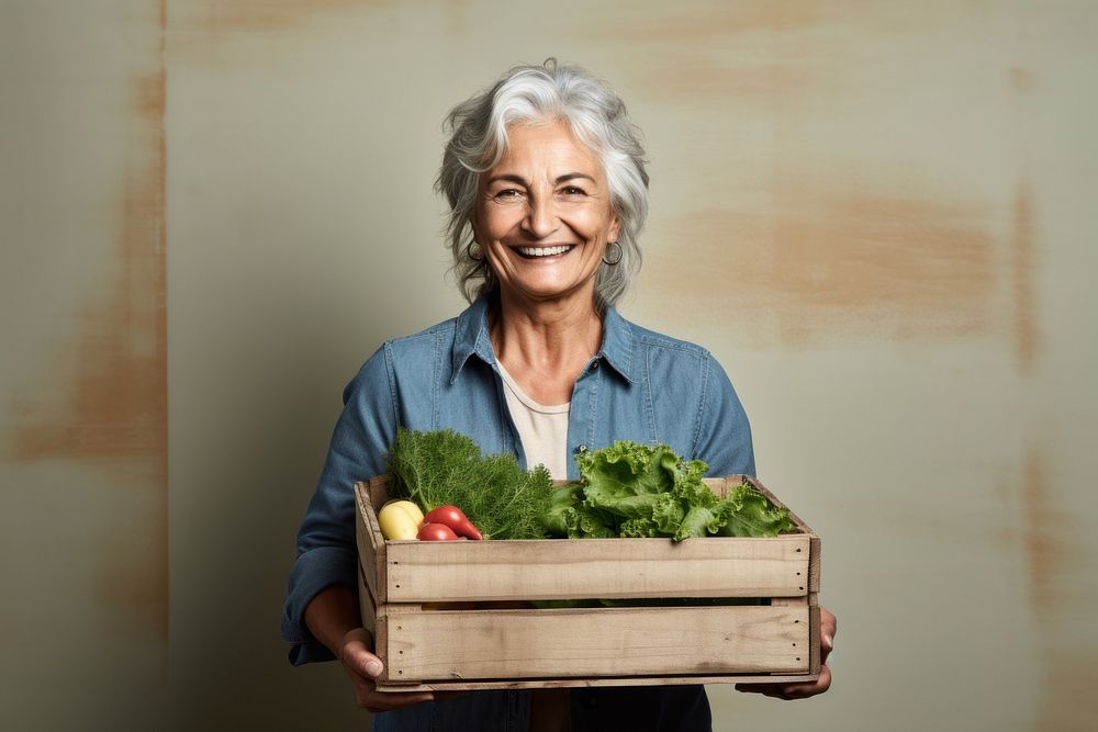 Old woman farmer smiling holding vegetable crate gardening outdoors produce.