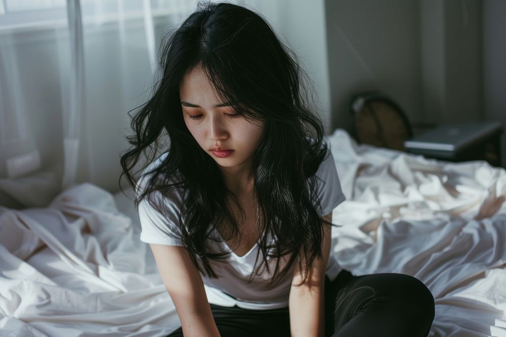 Asian girl looking tired sitting on bed worried adult disappointment.