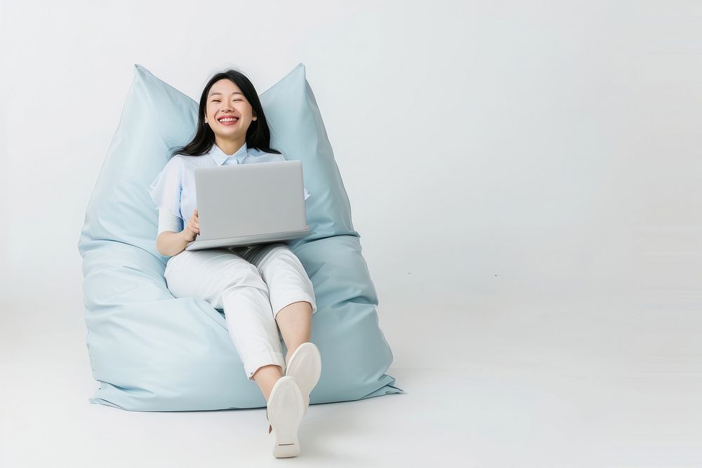 Cheerful asian woman working on laptop seated on a minimal luxury color beanbag furniture computer cheerful.