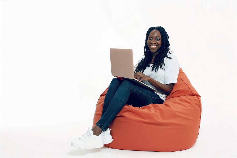 Cheerful black woman working on laptop seated on a minimal luxury color beanbag furniture computer cheerful.