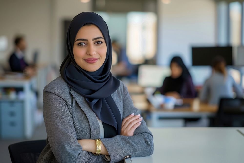 Confident Middle Eastern businesswoman leaning on desk in office executive clothing apparel.