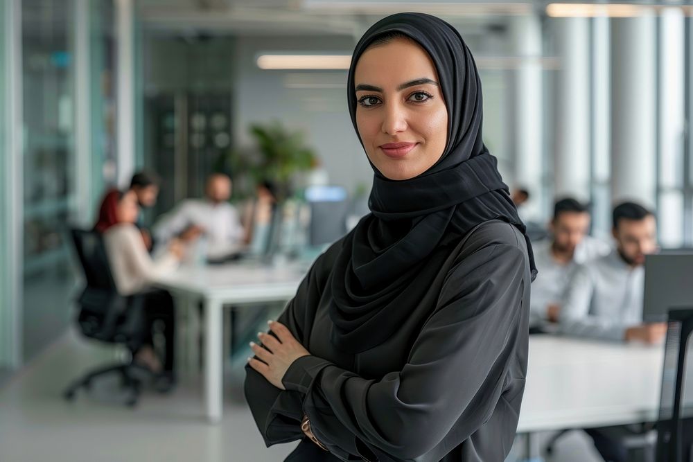Confident Middle Eastern businesswoman leaning on desk in office executive clothing apparel.