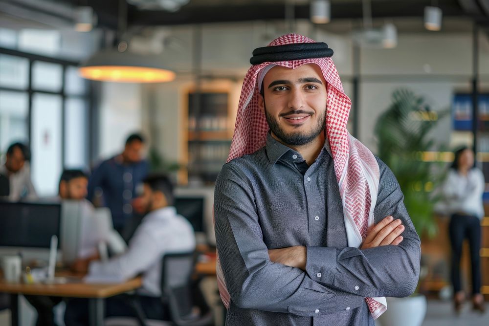 Confident Middle Eastern businessman leaning on desk in office electronics executive clothing.