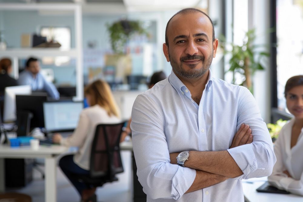 Confident Middle Eastern businessman leaning on desk in office electronics wristwatch executive.