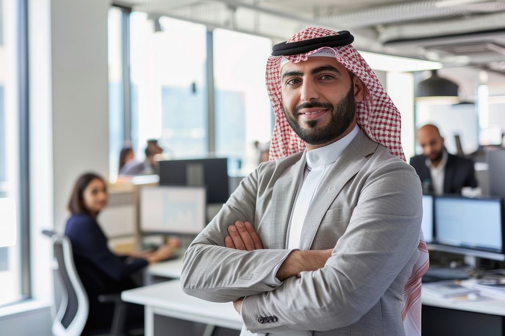 Confident Middle Eastern businessman leaning on desk in office electronics executive furniture.