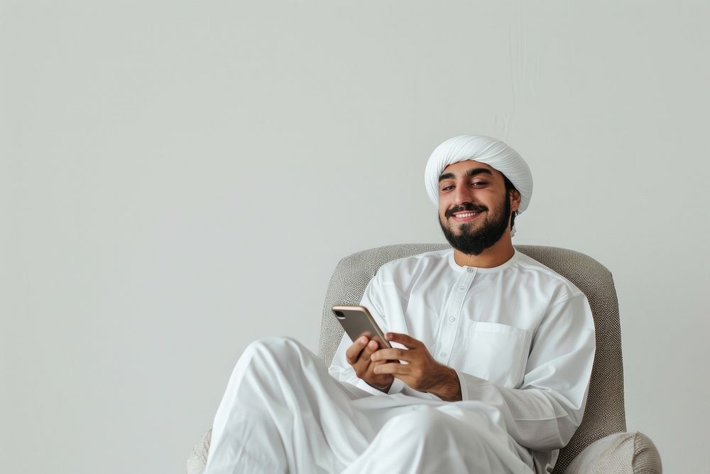 Joyful young male Middle Eastern sitting in armchair with smartphone person human adult.