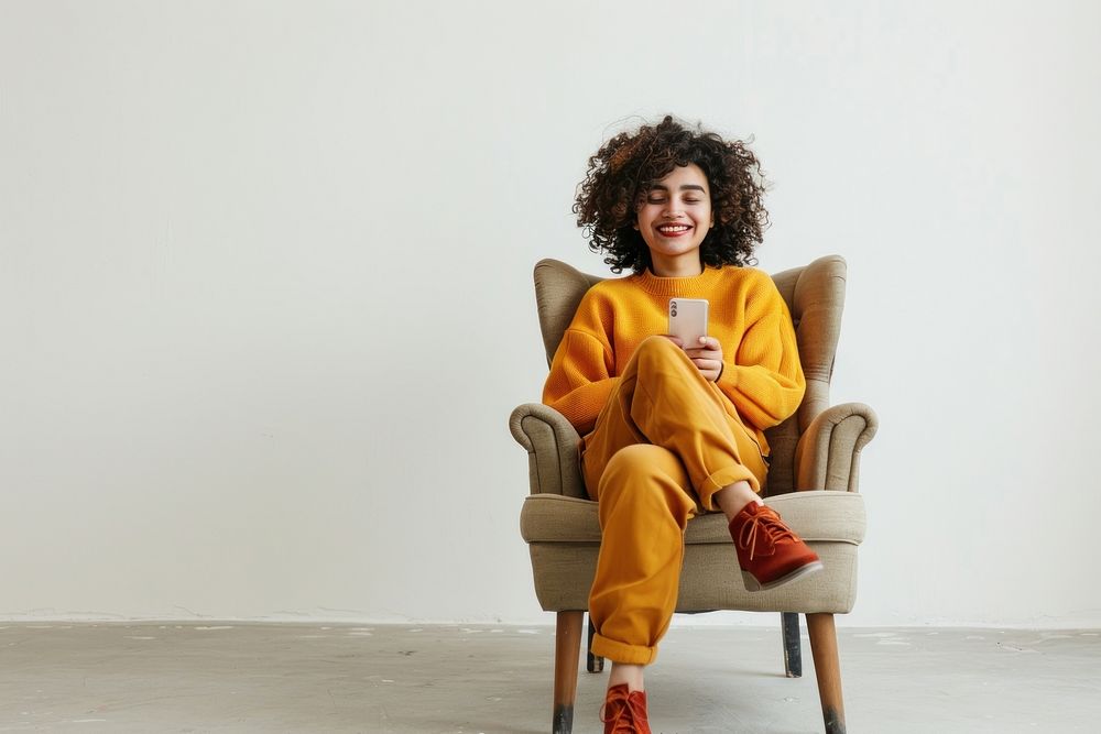 Joyful young Middle Eastern sitting in armchair with smartphone furniture person human.