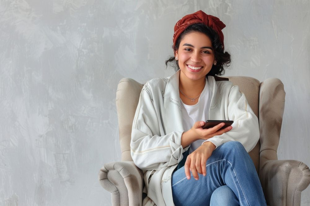 Joyful young Middle Eastern sitting in armchair with smartphone accessories accessory furniture.