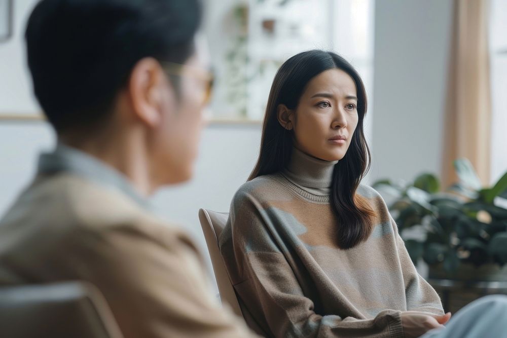 An asian female psychologist sit opposite to a man patient conversation clothing knitwear.