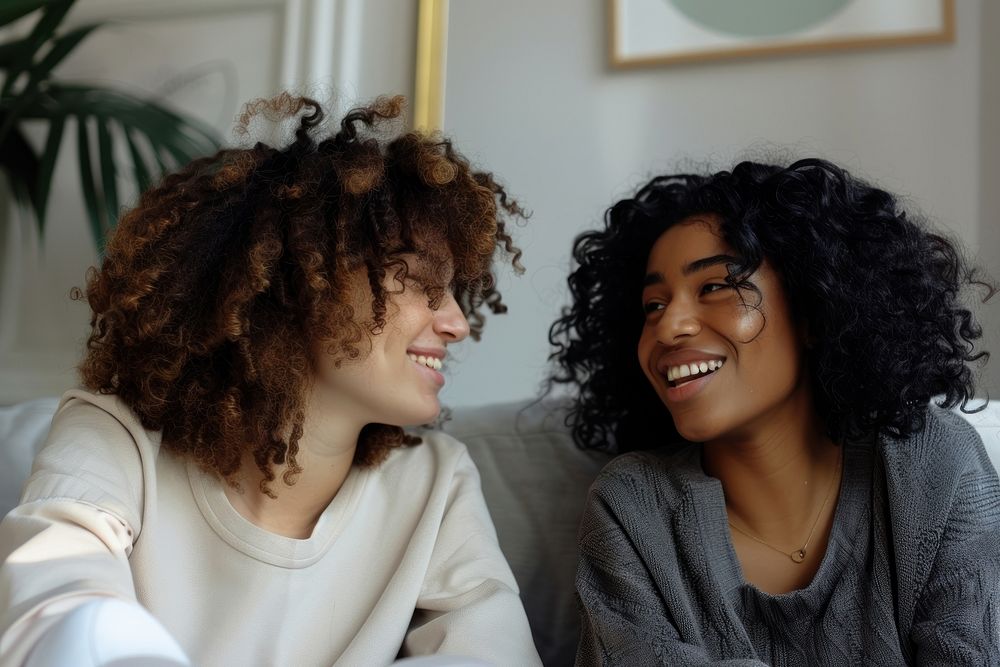 Two female friends sitting on a couch and talking accessories accessory laughing.