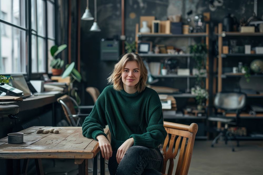 Focus on a short hair woman in green sweater turn sideway to smile at camera sitting electronics clothing.