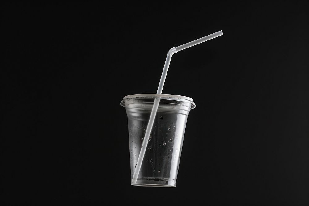 Clear plastic coffee cup and cap and straw glass black background refreshment.