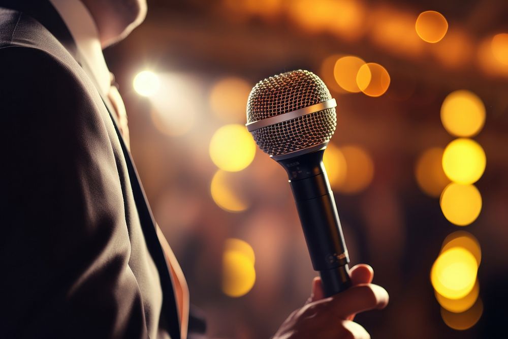 Motivational speaker with microphone performing on stage adult night illuminated.