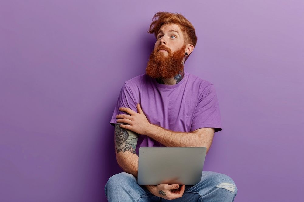 Full body young redhead bearded man in violet t-shirt casual clothes sitting hold use work on laptop pc computer point aside…