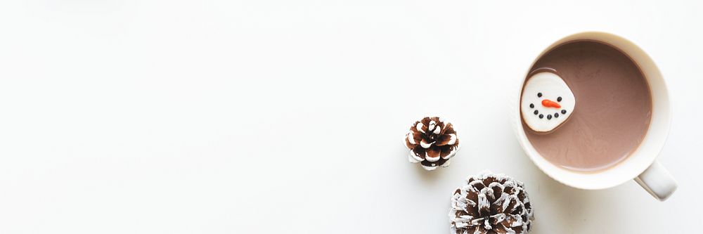 Cup of hot chocolate with a snowman marshmallow, surrounded by pinecones on a white background. Cozy winter vibes with hot…