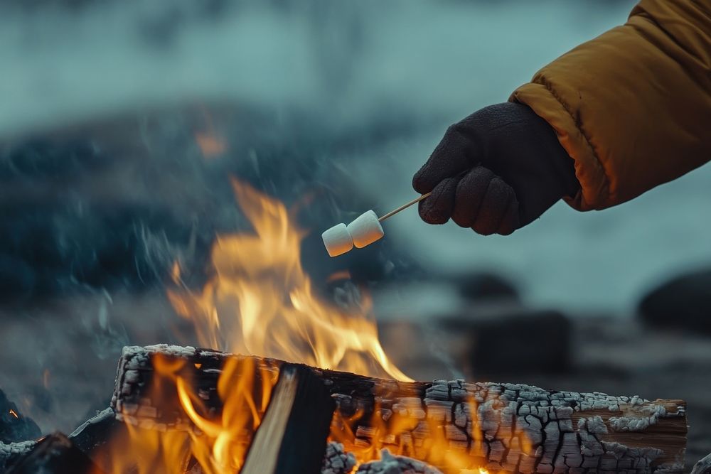 Hand roasting marshmallows over the bonfire flames campfire outdoors.