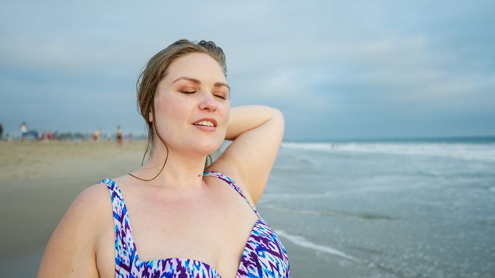 Curvy woman enjoying the beach, eyes closed, feeling the breeze. Relaxed woman at the beach, wearing a patterned swimsuit…