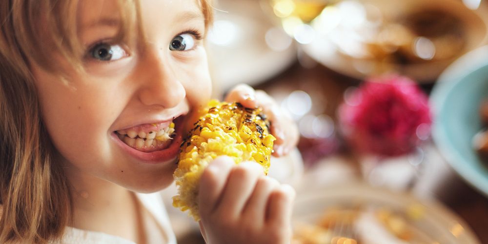 Child enjoying grilled corn, smiling while eating corn. Happy child with corn, close-up of corn and child. Corn and child at…