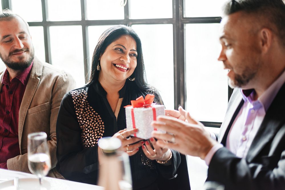 Group of people exchanging gifts at a celebration. Smiling woman receiving a present. Joyful atmosphere with friends sharing…