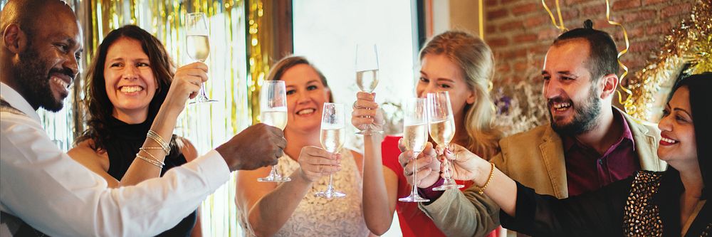 Group of diverse friends celebrate with champagne. Diverse colleague friends toasting at office party with decorations and…