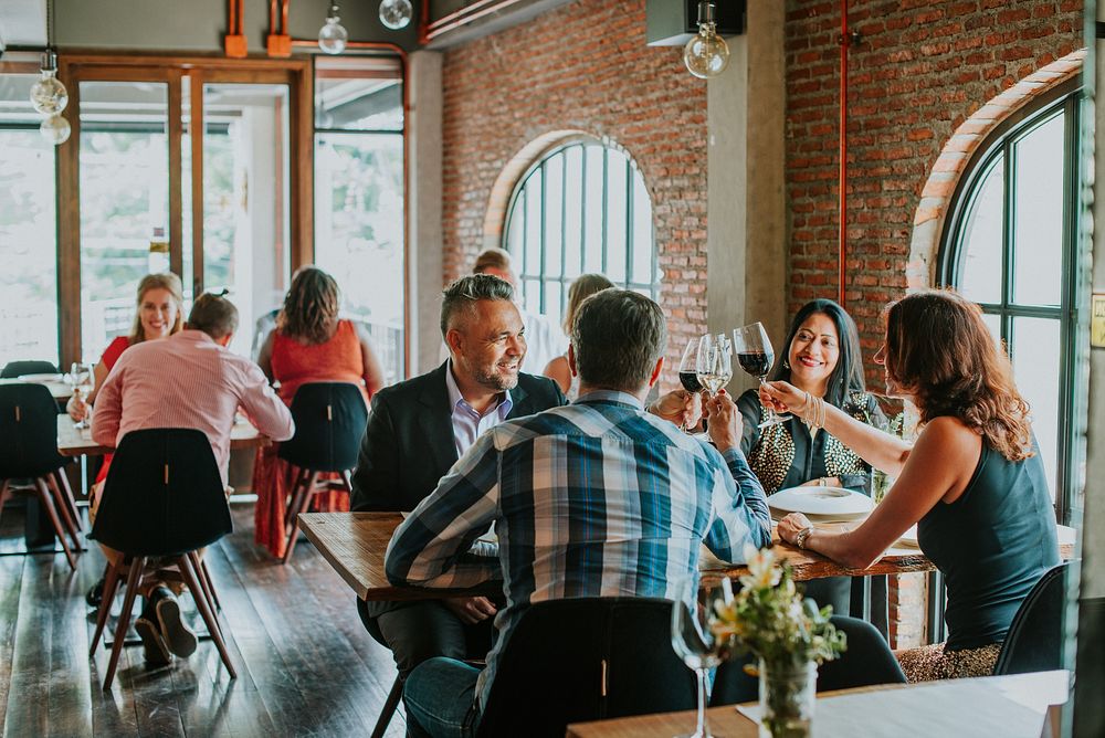 Group dining in a cozy restaurant. Friends enjoying a meal, sharing laughter. Warm ambiance, brick walls, large windows.…