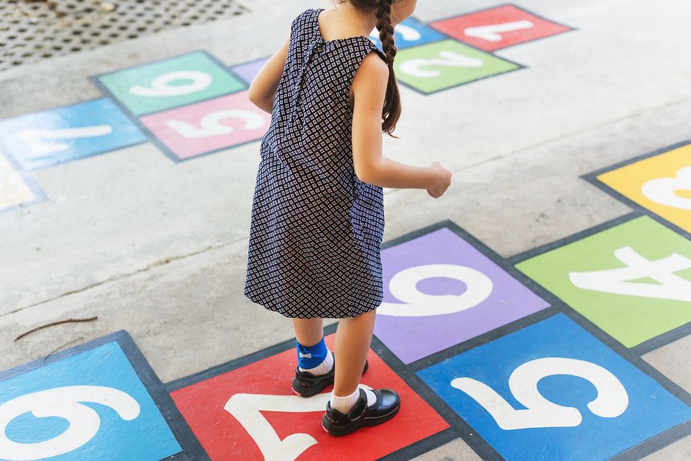 Child playing hopscotch on colorful numbered squares. Girl in dress, outdoor game, hopscotch fun. Bright numbers, playful…