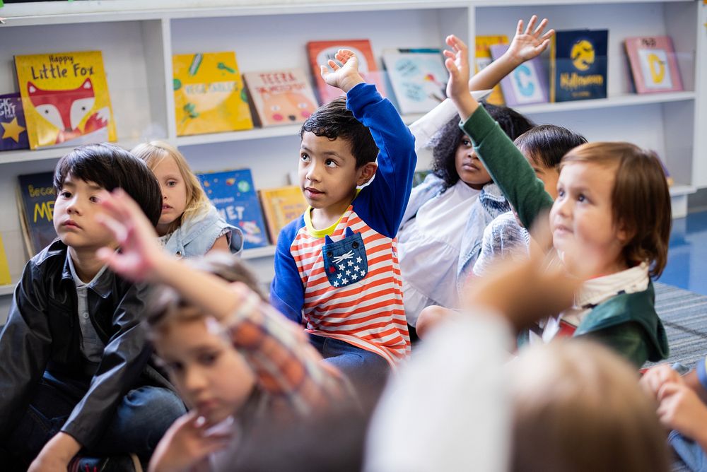 Children in a classroom raising hands. Diverse group of kids, including boys and girls, engaged in learning. Classroom…