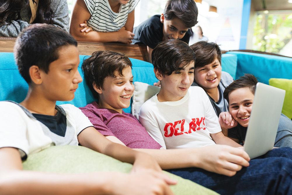 Group of boys, diverse ethnicities, gathered around a laptop, smiling and engaged. Boys enjoying technology, boys sharing a…