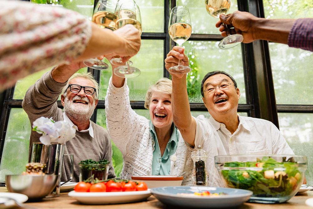 Diverse senior friends enjoying meal together, toasting drinks. Diverse elderly toasting drinks, eating healthy meal at…