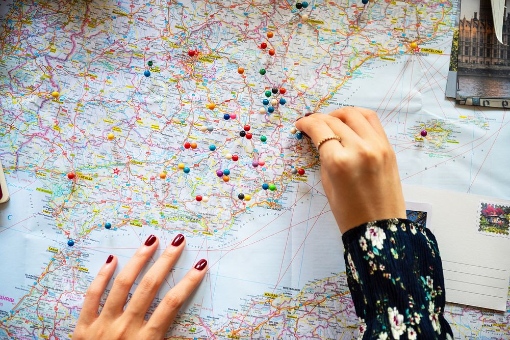 A close-up of a woman's hand, possibly placing colorful pins on a detailed map. The map features various locations…