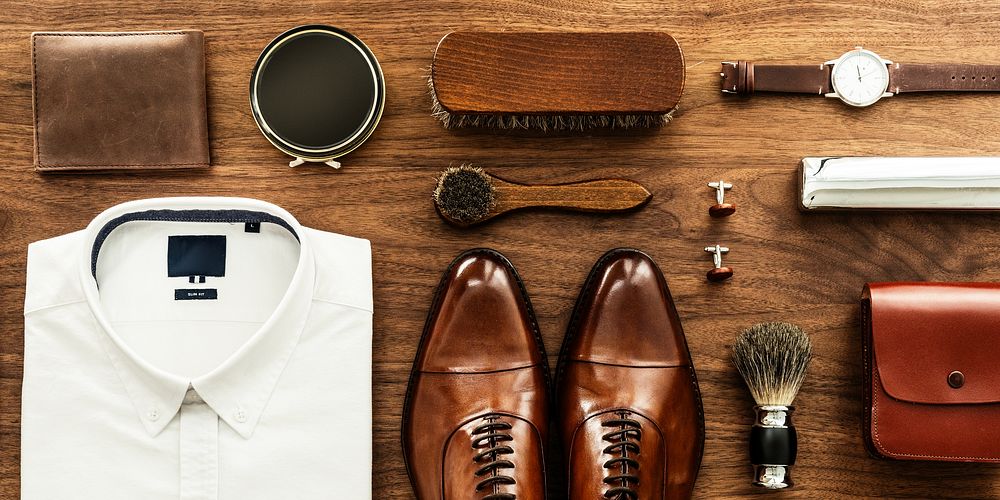 A stylish men's outfit flat lay featuring a white shirt, brown shoes, a tie, and accessories. This men's fashion display…